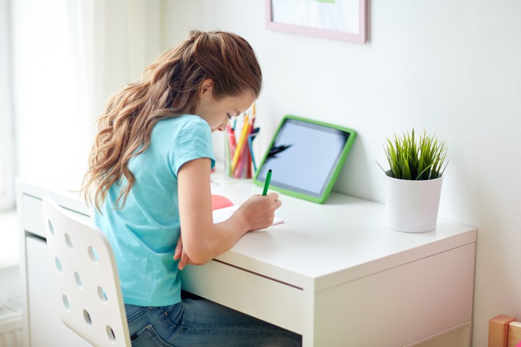 girl with tablet pc writing to notebook at home